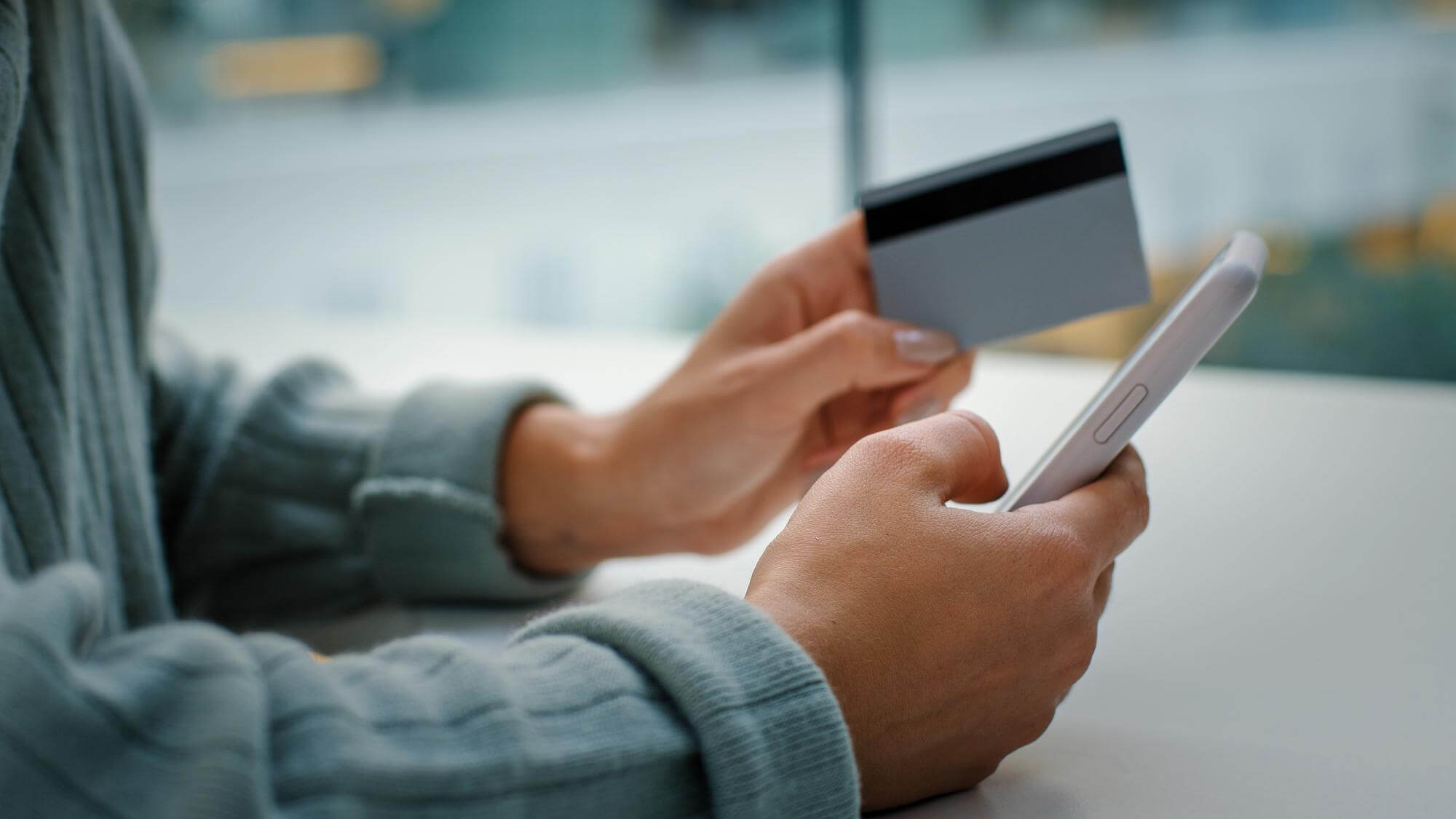 Mann schaut auf Handy mit Kraditkarte in der Hand