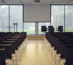 Rear view of seats and passage in a conference hall, projection screen in background, no people, copy space.